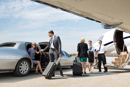 Chauffeur meeting corporate executives at their limo and helping to transport luggage to a private jet at the airport
