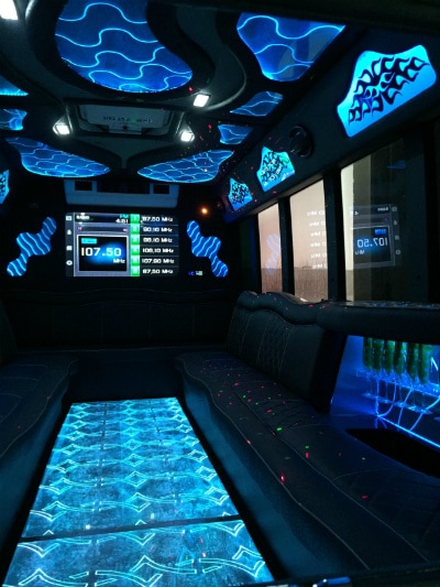 Amazing interior picture of 22 passenger limo bus with custom, color changing lighting and disco floor. A large flat panel DirecTV connected TV is visible on the back wall.